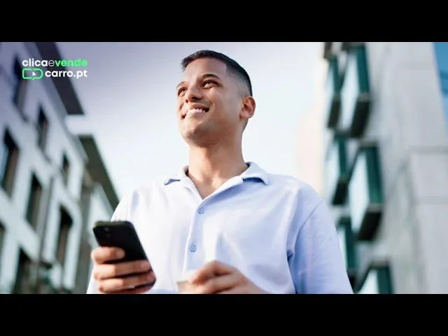 Hombre joven sonriendo mientras usa su teléfono móvil para vender su coche en Clica e Vende Coche